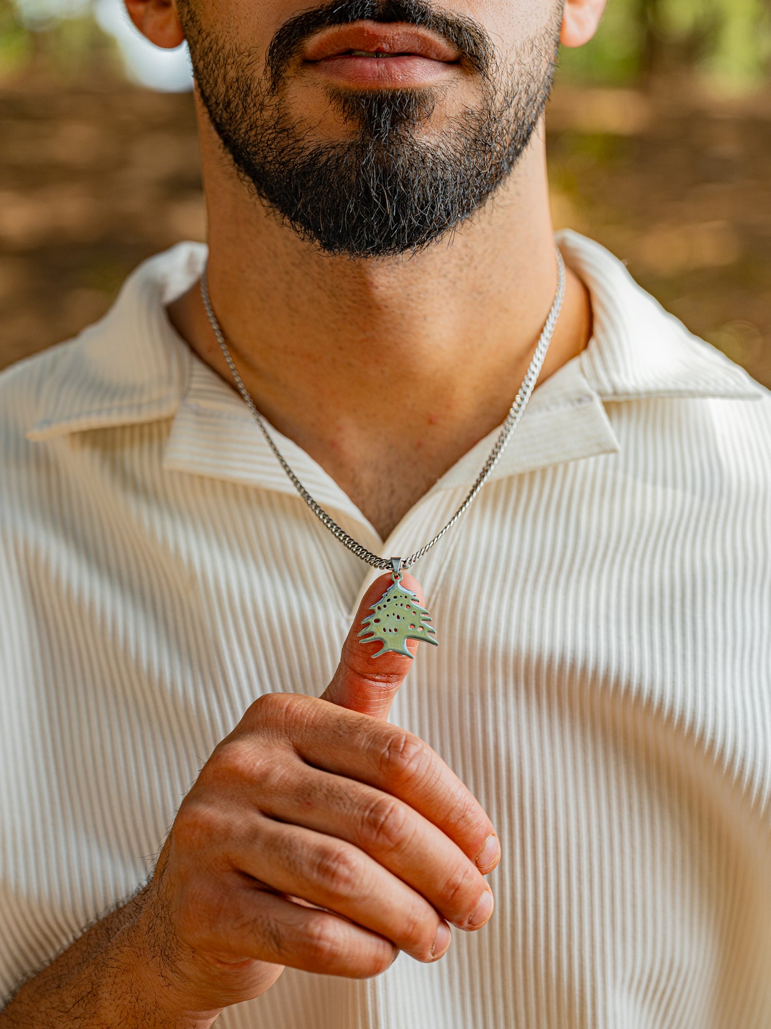 Man wearing a necklace with a lebanese cedar tree icon pendant outdoors